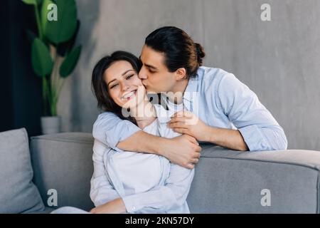 Il conforto amorevole del marito ha offeso la moglie, carezzandola e abbracciandola da dietro. L'uomo premuroso che fa pace e riconcilia con il suo amato, mostrando sup Foto Stock