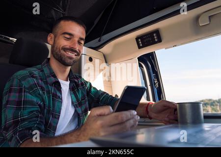 uomo che usa il telefono cellulare e il computer portatile dal suo camper Foto Stock