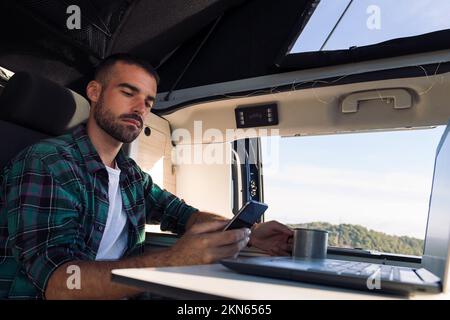 uomo che usa il telefono cellulare e il computer portatile dal suo camper Foto Stock