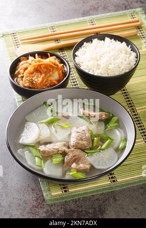 Zuppa di rafano di manzo coreano Sogogi Muguk servita con riso e kimchi closeup sul tappeto sul tavolo. Verticale Foto Stock