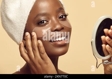 La ragazza afroamericana mette sotto gli occhi le zone sul fronte prima dello specchio. Foto Stock