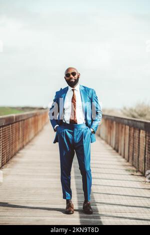 Fuoco selettivo su un Signore africano calvo alto in un vestito blu con una cravatta marrone modellata per abbinare i suoi pattini; un uomo nero-bearded elegante che indossa su Foto Stock