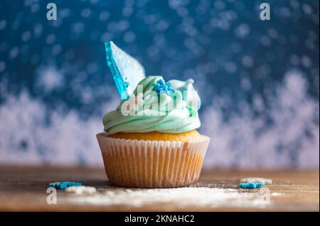 Cupcake fatto in casa di colore blu collocato su una scrivania di legno. Tema invernale e natalizio, fiocchi di neve al gelato blu. Dolce fresco e cotto in casa. Foto Stock