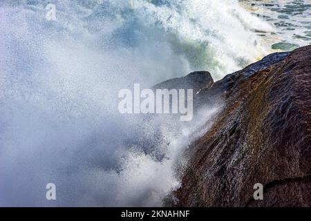 Grande onda che si schiantano contro le rocce con acqua di mare che spruzzi in aria durante la tempesta Foto Stock