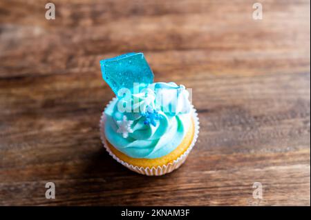 Cupcake fatto in casa di colore blu collocato su una scrivania di legno. Tema invernale e natalizio, fiocchi di neve al gelato blu. Dolce fresco e cotto in casa. Foto Stock
