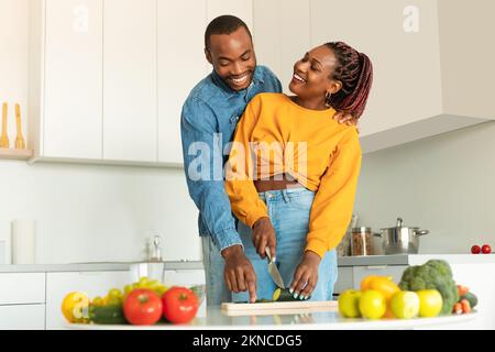 Romantici sposi neri che cucinano un pranzo sano a casa, felice uomo e donna che si gustano insieme gustosi piatti Foto Stock