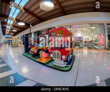 Cuneo, Italia - 18 novembre 2022: Zona giochi con carosello a forma di autobus a due piani rosso per giocare in un centro commerciale italiano. Foto Stock