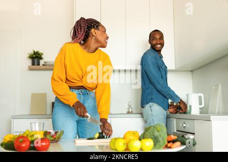 Felice coppia afro-americana preparare cibo sano, trascorrere il tempo in cucina insieme, parlando durante la cucina Foto Stock