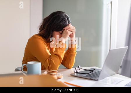 Burnout remoto. Giovane donna araba depressa seduta alla scrivania con laptop Foto Stock