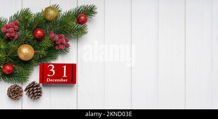 Ramo d'albero di Natale con decorazione, due coni di abete e calendario perpetuo rosso con data 31 dicembre su sfondo bianco in legno. Vista dall'alto, piatto con c Foto Stock