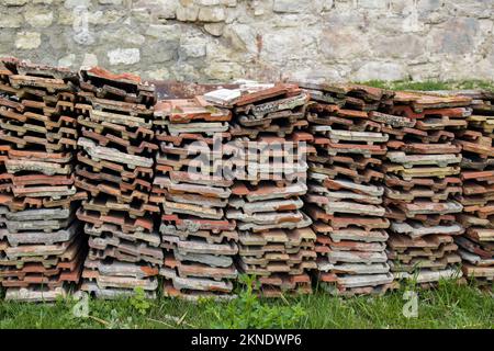 Vecchie piastrelle di argilla sono impilate su erba verde, sullo sfondo di vecchio muro di pietra. Spazio di copia. Messa a fuoco selettiva. Foto Stock