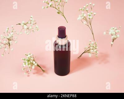 Bomboletta spray cosmetica marrone senza marchio e fiori di gypsofila volanti su sfondo rosa. Cosmetici naturali biologici spa. Nebbia corporea, Mockup, template. Foto Stock