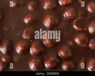 Gustoso cioccolato fondente con nocciole sullo sfondo, vista dall'alto delle nocciole fuse nel cioccolato fondente Foto Stock