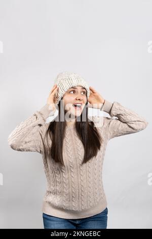 Una donna in un cappello invernale e maglione tiene le mani sulla testa e urla guardando lontano. Foto Stock