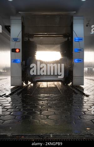 L'auto viene lavata in un autolavaggio automatico coperto con programma di lavaggio. Effetto luce solare. Lavaggio auto. Spazzole rotanti sopra e accanto all'auto Foto Stock