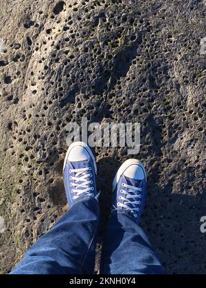 Il punto di vista della persona che guarda giù sulle scarpe mentre si alza su una roccia Foto Stock
