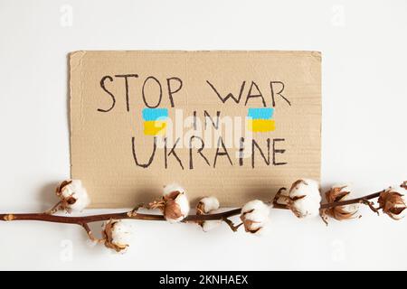 Fermare la guerra in Ucraina è scritto su carta e accanto ad essa si trova un ramo di cotone su uno sfondo bianco, un'azione di protesta 2022 Foto Stock