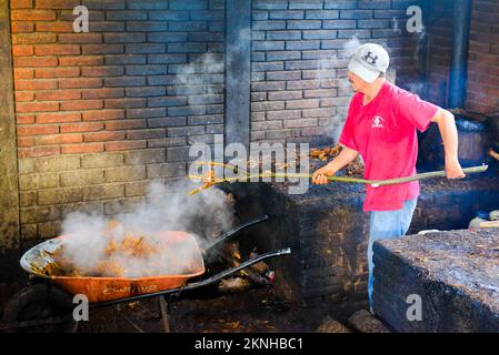 Dopo il primo processo di distillazione dei cuori di agave schiacciati, la purea calda viene rimossa manualmente , distilleria artigianale Mezcal , Oaxaca Mexico Foto Stock