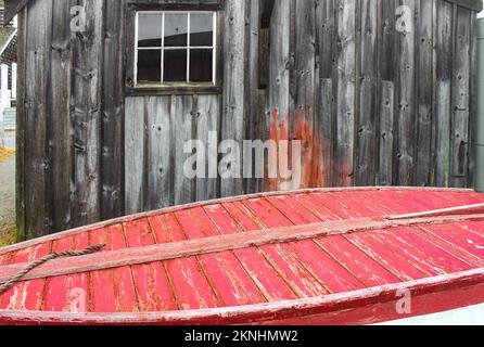 Vicino al mare - Vecchio edificio stagionato dietro il fondo di una barca di legno dipinta di rosso con una corda Foto Stock