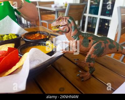 Dinosauro giocattolo si affaccia su chip antipasto nel ristorante messicano Foto Stock