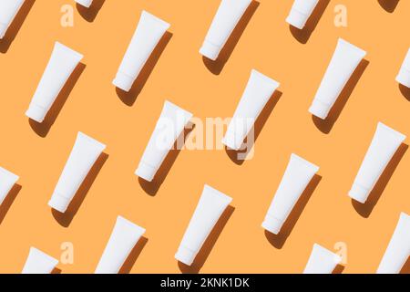 Modello realizzato con tubi bianchi di crema solare, crema per le mani o lozione per il corpo su sfondo arancione. Stile piatto, immagine mockup Foto Stock