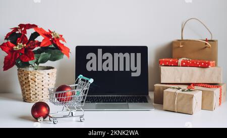 Stagione di Natale riuscita in e-Commercio, shopping in linea di Natale. Computer portatile aperto schermo, mini carrello, poinsettias Natale Foto Stock