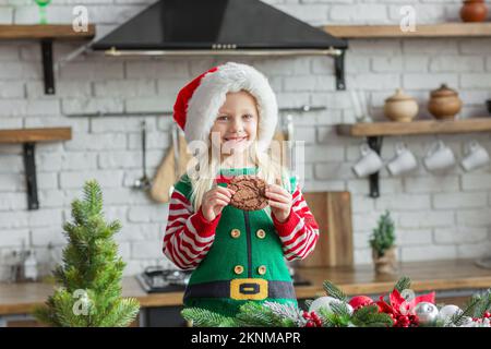 Ragazza in babbo natale cappello sorridente e mangiare biscotto di Natale Foto Stock