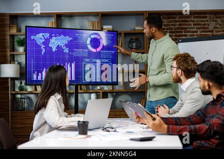 Motivata afroamericana imprenditore avere incontri d'affari con i manager, negoziare, utilizzando la presentazione tv con statistiche, grafici, big data Foto Stock