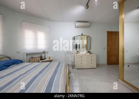 Vecchia camera da letto con pavimenti in gres, un letto con una cornice in metallo dorato e un armadio a muro con porte a specchio e bordi cromati dorati Foto Stock