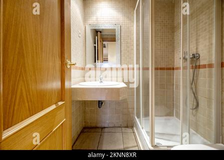 Piccolo bagno con cabina doccia con porte in vetro e finiture bianche, piano lavabo in marmo e piastrelle Foto Stock