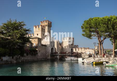 Sirmione, Italia - 25 giugno 2022: Castello Scaligero con Lago di Garda, piccolo battello e albero. Bella vista della Fortezza nel Nord Italia con il Cielo Blu. Foto Stock