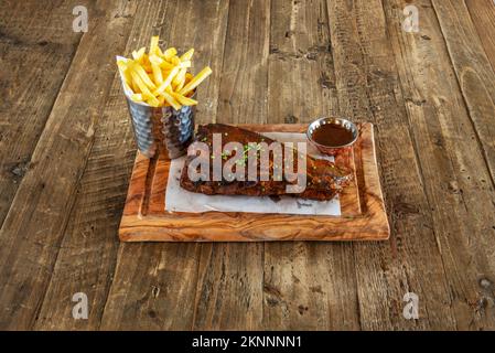 Un piatto meraviglioso di costolette di maiale alla griglia con salsa alla griglia sulla superficie, all'interno di un piccolo contenitore e di un altro contenitore metallico con patatine sfuse Foto Stock