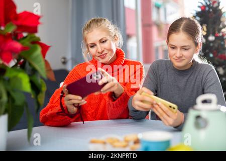 Figlia e mamma scrivono messaggi di saluto al telefono durante le vacanze di Natale Foto Stock