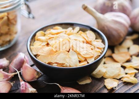 Ciotola di fiocchi d'aglio secchi. Teste di aglio e bicchiere di vetro di fiocchi d'aglio sullo sfondo. Condimento essiccato. Foto Stock