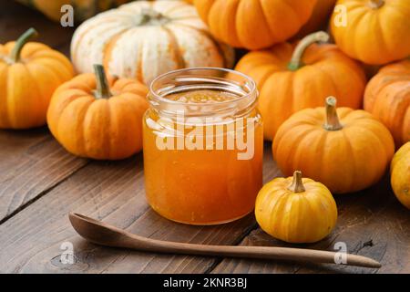 Vasetto di marmellata di zucca sana e cucchiaio di legno. Zucche sul tavolo da cucina. Foto Stock