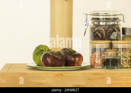 Vasetti di vetro di diverse dimensioni riempiti di spezie, condimenti, pasta per zuppe e chicchi di caffè, un vasetto di bambù e alcuni deliziosi pomodori in un legno di bambù Foto Stock