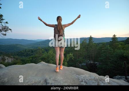 Donna escursionista che si rilassa sul sentiero di montagna alzando le mani godendo la natura serale durante il viaggio su sentiero natura selvaggia. Solitario viaggiatore femminile Foto Stock