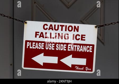 Un cartello rosso e bianco Caution Falling Ice su una catena sul portico anteriore di un edificio che indica al traffico di utilizzare l'ingresso laterale. Foto Stock