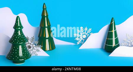 Alberi di Natale in ceramica, neve di carta e fiocchi di neve su sfondo azzurro Foto Stock