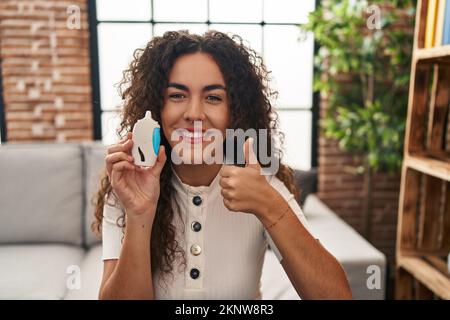 Giovane donna ispanica utilizzando glucometro sorridente felice e positivo, pollice su facendo eccellente e segno di approvazione Foto Stock