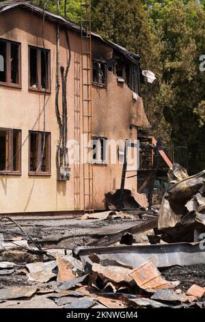 Fuoco danneggiato casa stile cottage vicino ai resti di edificio commerciale bruciato. Foto Stock