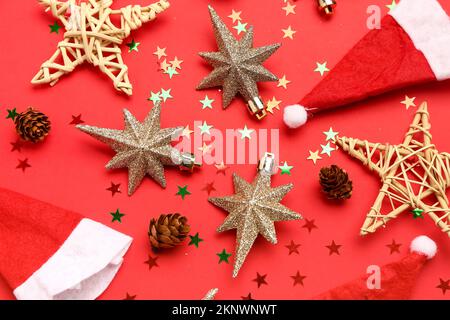 Composizione con decorazioni natalizie, cappelli e coni di Santa su sfondo rosso Foto Stock