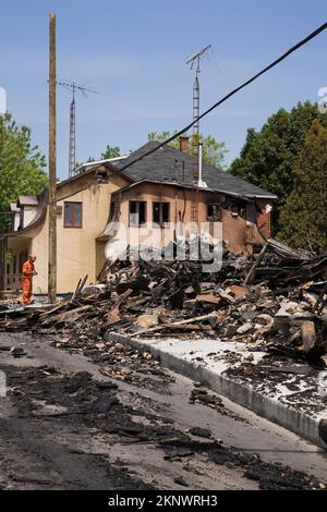 Pulisca-in su il lavoratore vicino alla casa danneggiata di stile del cottage del fuoco con i residui di un edificio commerciale bruciato. Foto Stock