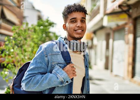 Il giovane ispanico sorride indossando le cuffie per strada Foto Stock