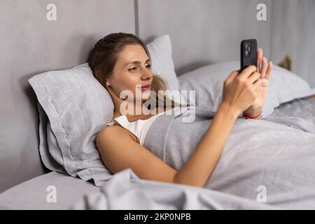 Vista dall'alto donna risvegliata sdraiata nel letto tiene smartphone guarda lo schermo guardando il tempo di oversleped e si sente stressato, stravolto femmina letto ricevuto awf Foto Stock