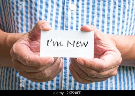 Uomo che tiene un biglietto da visita bianco con le parole, sono nuovo. Foto Stock