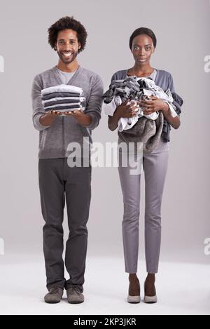 Ho vinto. Studio shot di un uomo che tiene una pila di vestiti ben ripiegata mentre i suoi partner sono in un pasticcio. Foto Stock