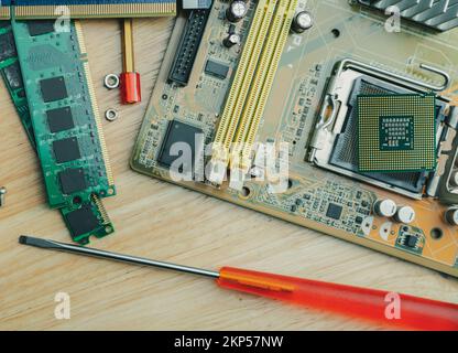 Chip del computer sulla scheda elettronica della scheda madre del PC e cacciavite presso l'officina di riparazione. Vista dall'alto del chipset della CPU sul tavolo. Componenti elettronici. Foto Stock