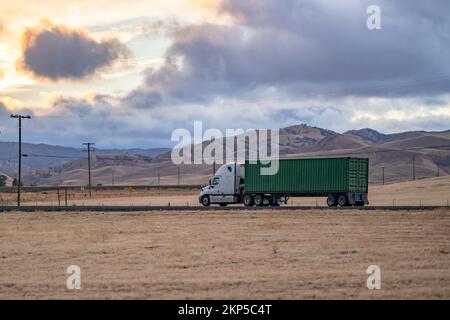 Potente semirimorchio bianco grande classico a lunga percorrenza con cabina alta per il trasporto di carichi pesanti in container di dimensioni normali sul semirimorchio in marcia Foto Stock