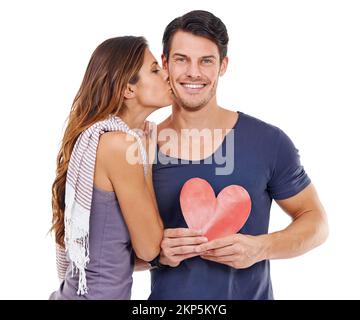 Per sempre e un giorno più uno. Studio shot di una giovane donna che bacia il suo ragazzo che sta tenendo un cuore. Foto Stock